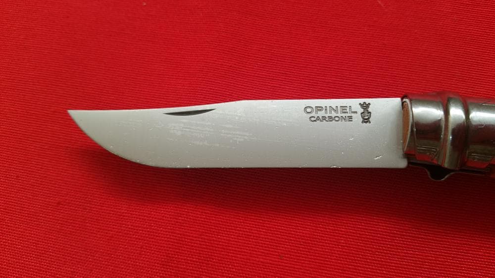 Detalle de hoja de navaja opinel abierta expuesta en tela roja. Vendida por Espadas y más