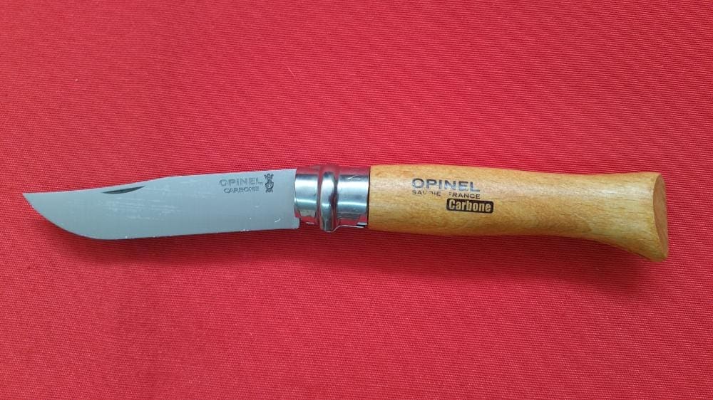 Navaja opinel con mango marrón abierta expuesta en tela roja. Vendida por Espadas y más