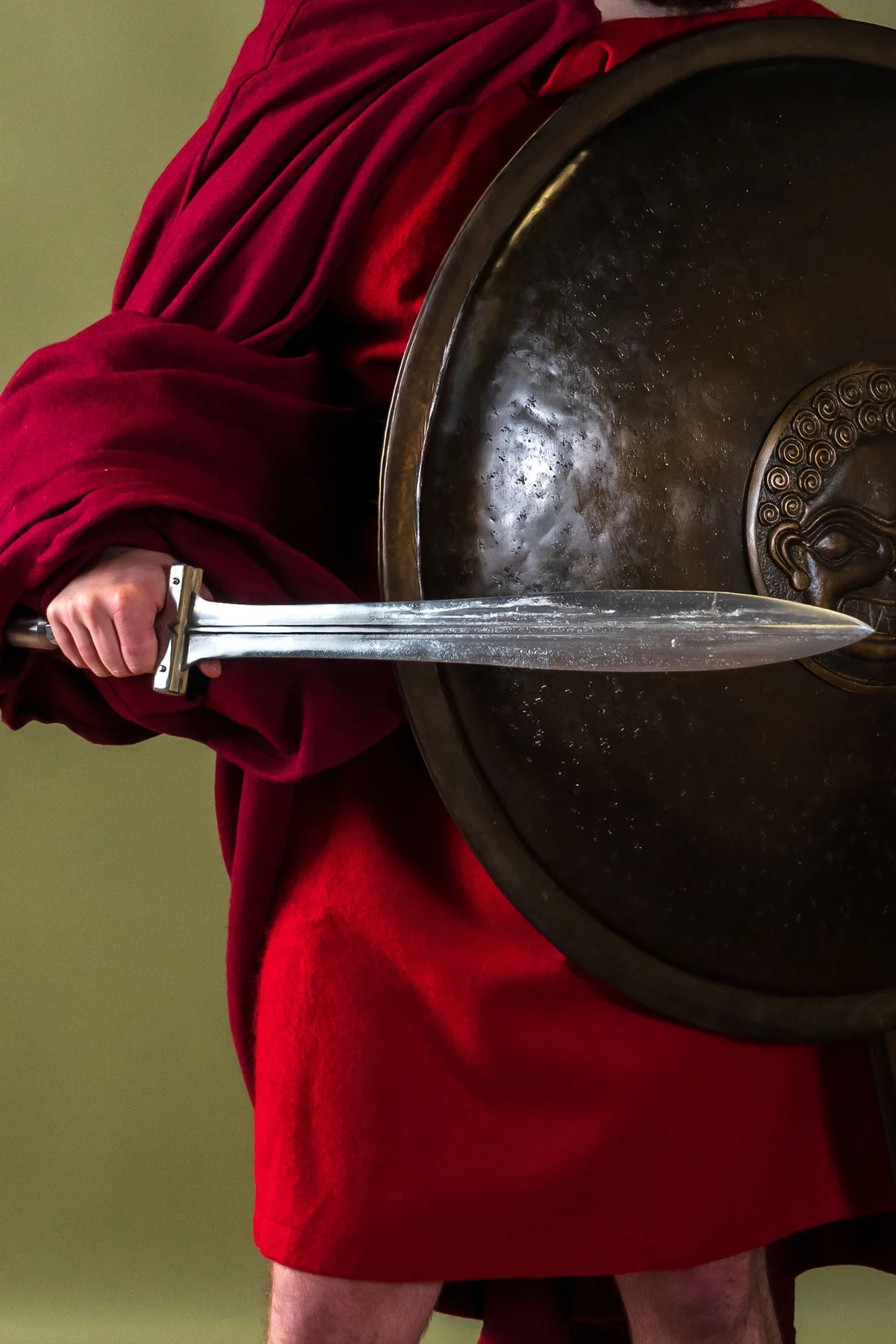 Persona sosteniendo un escudo redondo y una espada espartana